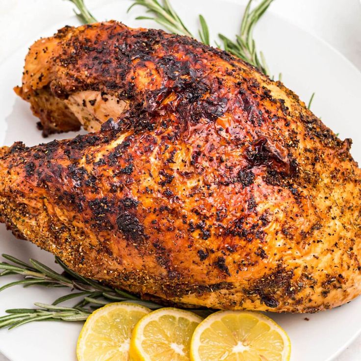 a whole chicken on a white plate with lemons and rosemary garnishes