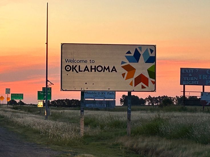 the welcome sign to oklahoma is lit up at sunset on an empty highway