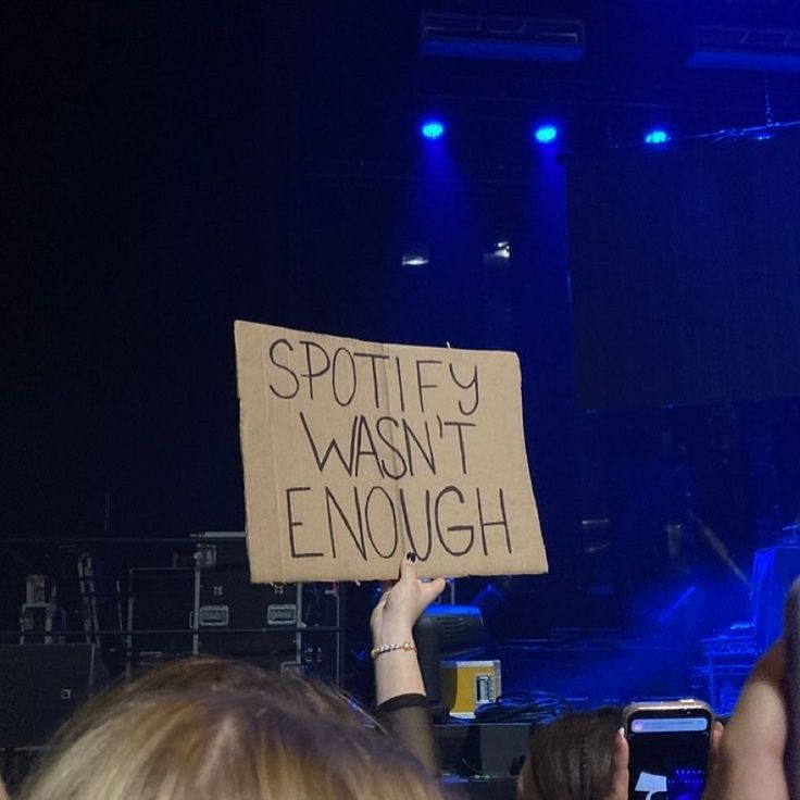 a person holding up a sign that says spotify hasn't enough