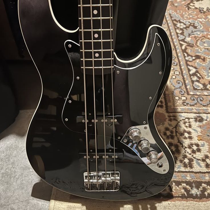 a black bass guitar sitting on top of a carpet