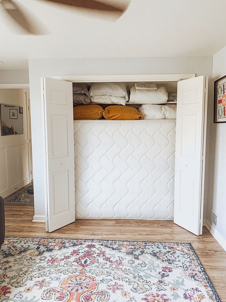 an open closet in the middle of a room with white doors and pillows on it