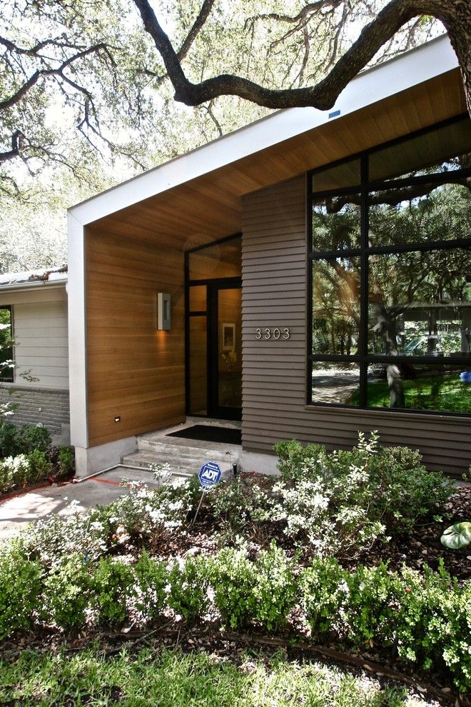 the front entrance to a modern home surrounded by trees and shrubs, with large windows on each side