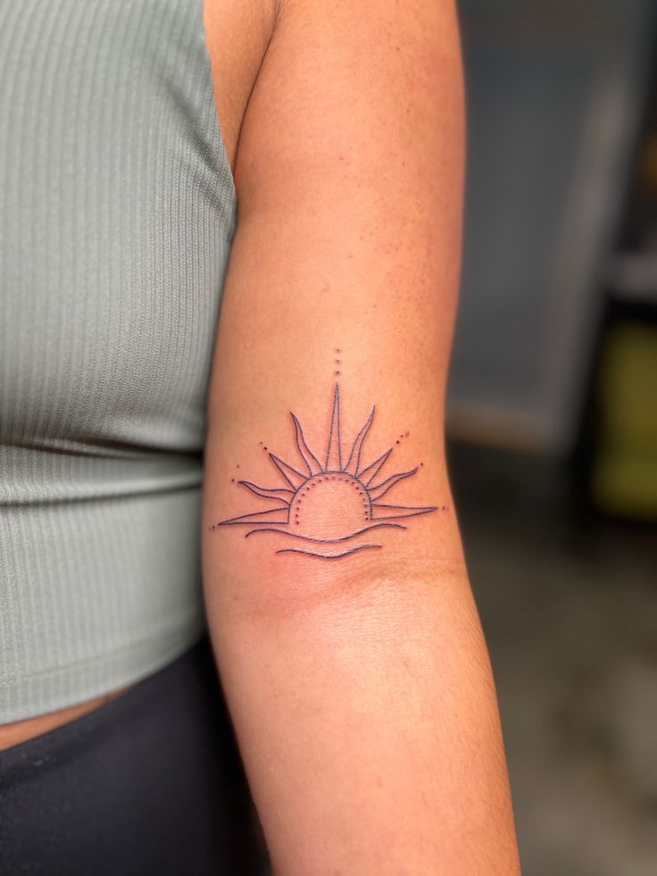 a woman's arm with a small sun tattoo on the left side of her arm