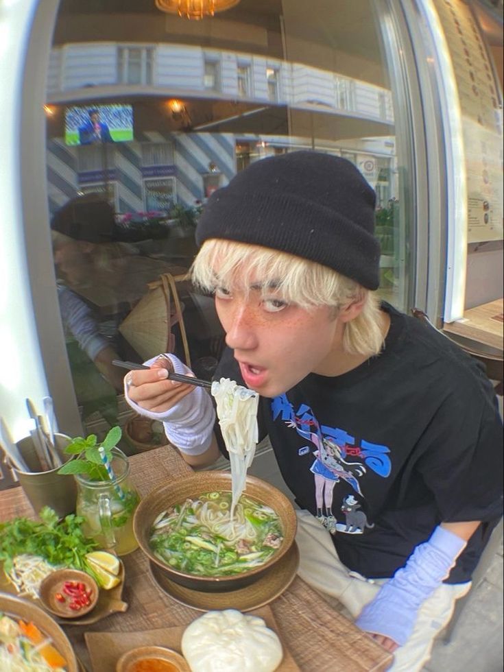 a person sitting at a table with bowls of food in front of them and eating noodles