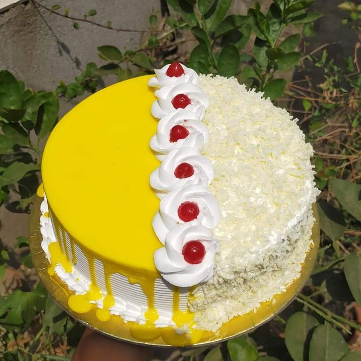 a yellow cake with white frosting and cherries on the top, sitting in front of green leaves