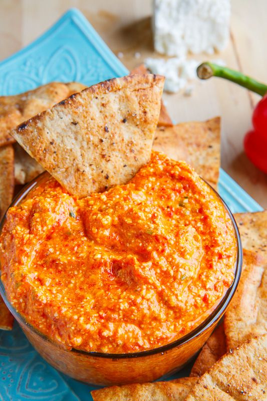 a bowl of dip with tortilla chips and tomatoes in the background on a blue plate