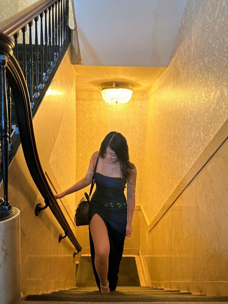 a woman in a black dress is walking down the stairs with her handbag on her hip