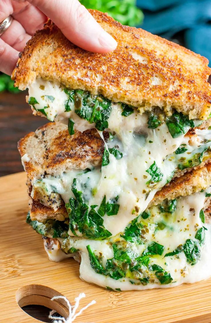 someone is holding up a grilled cheese and spinach sandwich on a cutting board