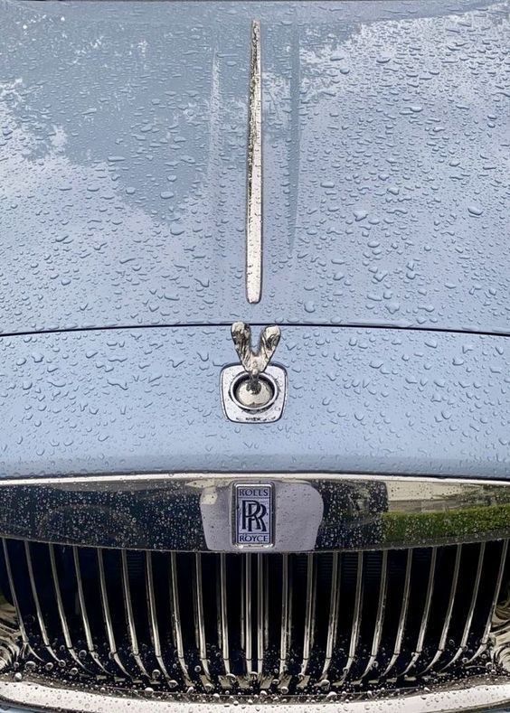 the front end of a blue car with water droplets on it's grills