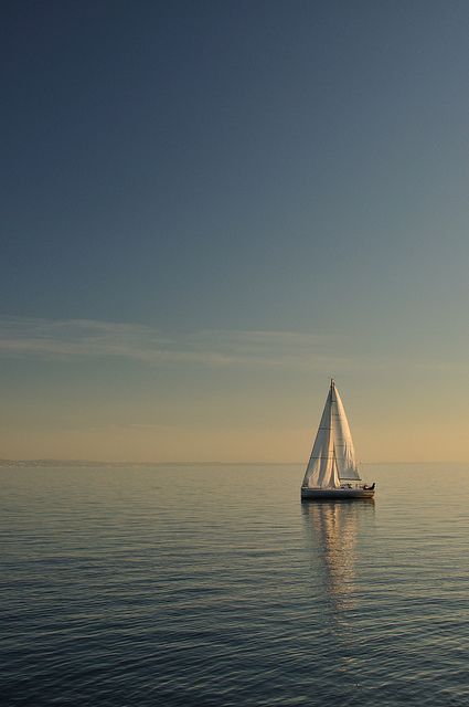 a sailboat floating in the middle of the ocean at sunset or sunrise, with no one on it