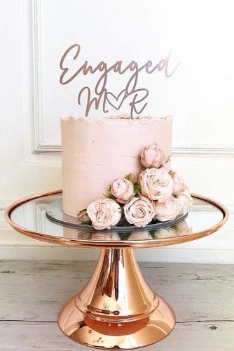 a pink cake with flowers on top sitting on a gold stand next to a white door