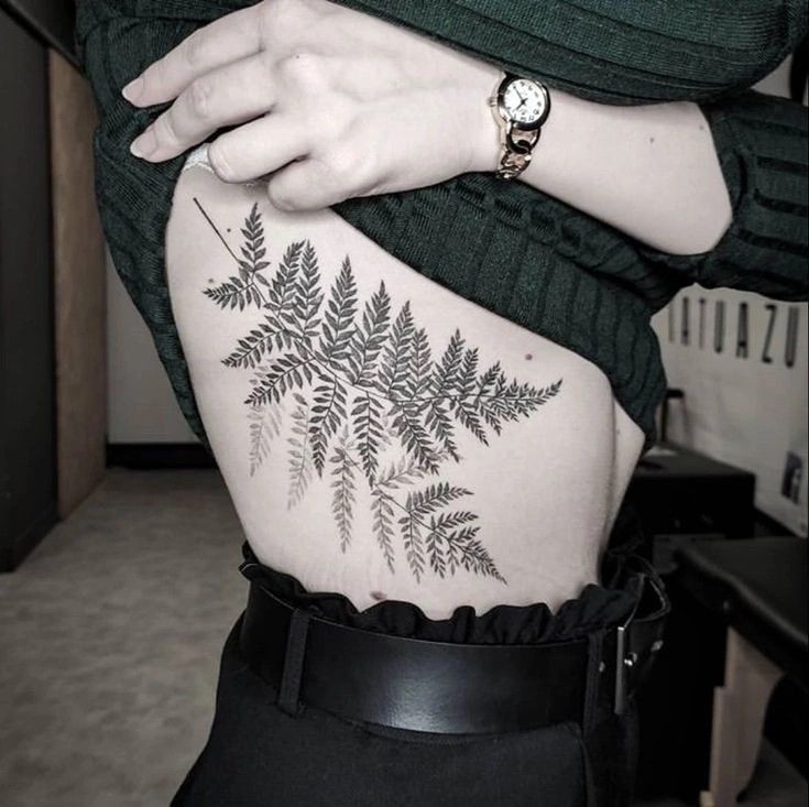 a woman's lower back tattoo with leaves on her stomach and a watch hanging from the wrist