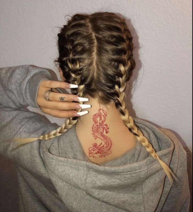 a woman with two braids in her hair and tattoos on her back shoulder is looking at the camera