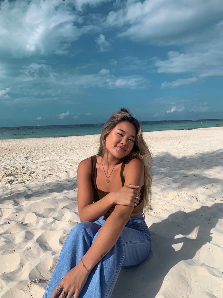 a woman is sitting on the beach with her arms crossed and looking at the camera