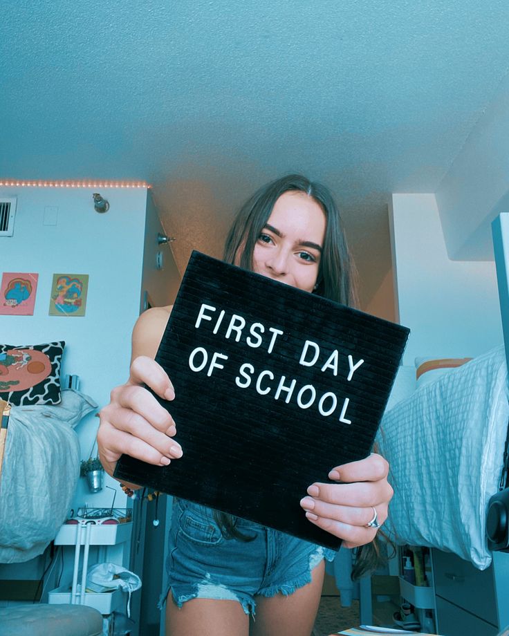 a woman holding up a sign that says first day of school in front of her face