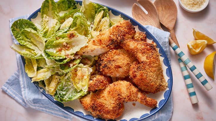 a blue and white plate topped with chicken, lettuce and lemon wedges