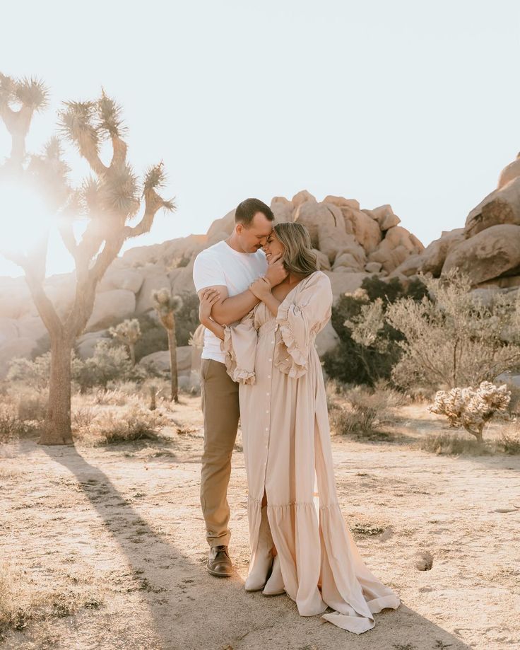 a man and woman standing in the desert with joshua tree behind them, hugging each other