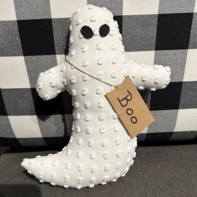 a white stuffed ghost sitting on top of a black and white checkered couch next to a tag