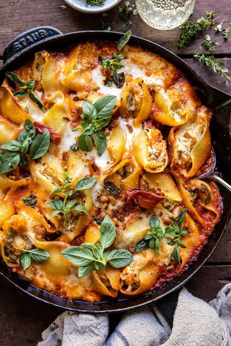 a skillet filled with pasta and sauce on top of a wooden table next to a towel