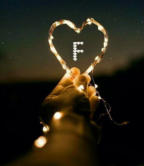 someone holding up a heart shaped light string with the letter f in it's center