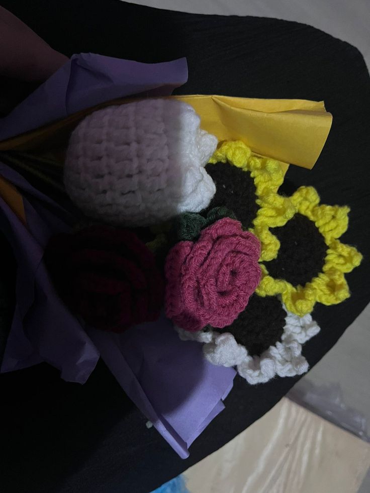 crocheted flowers are sitting on top of a black tablecloth with yellow and purple ribbons