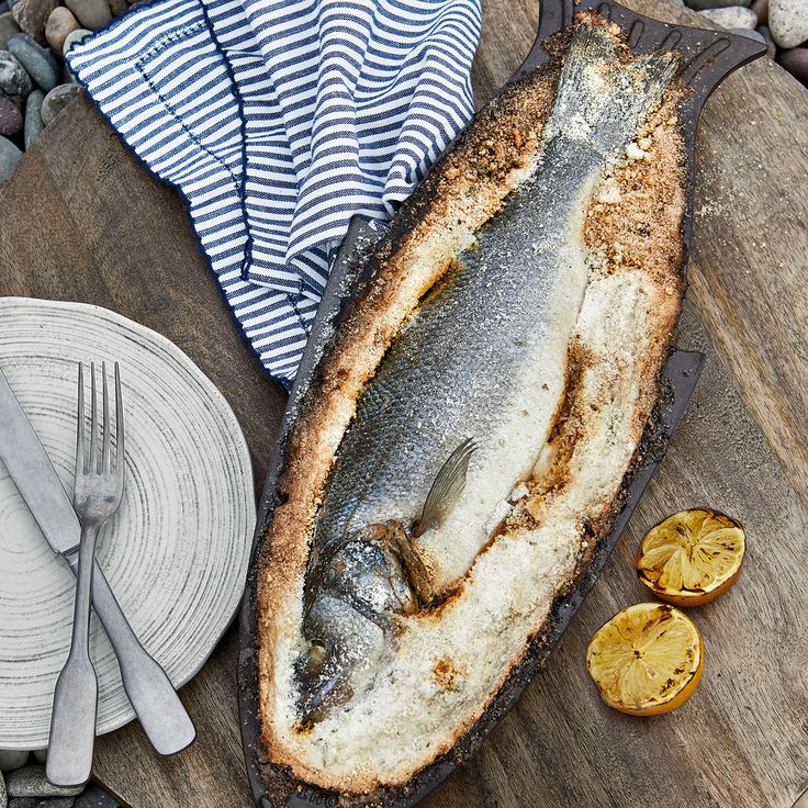 a fish is sitting on a wooden table next to some silverware and a plate