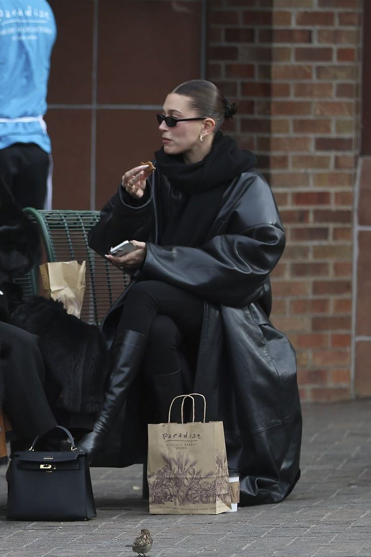 a woman sitting on a bench eating food and talking on her cell phone while holding a shopping bag