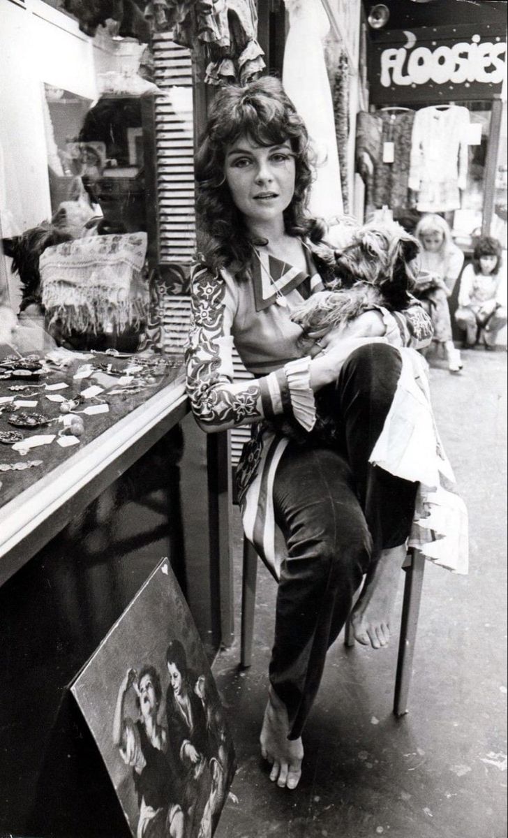 a woman sitting on a chair in front of a store holding a cat and looking at the camera