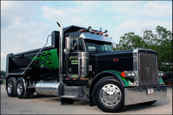 a green and black dump truck parked in a parking lot next to some trees on a sunny day