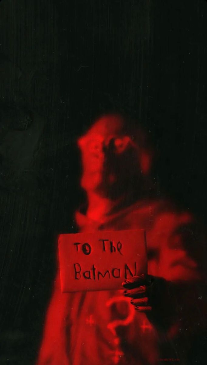 a man holding a sign that says to the batman on it in front of a black background