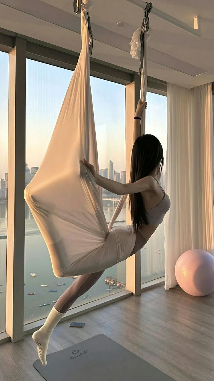 a woman is swinging on a hammock in front of a window with a city view