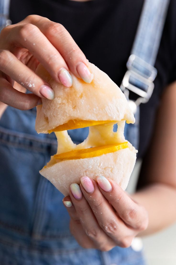 a woman holding a sandwich in her hands with cheese on it and an egg between the buns