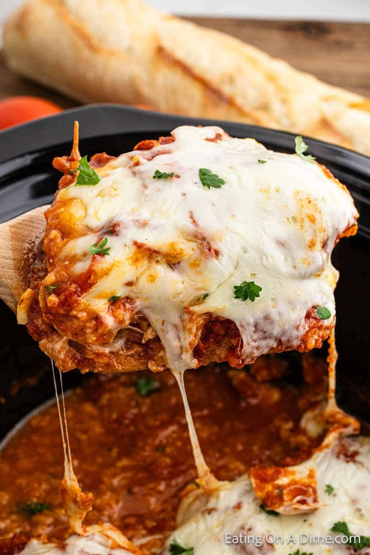 a wooden spoon full of lasagna sauce being lifted from a slow cooker