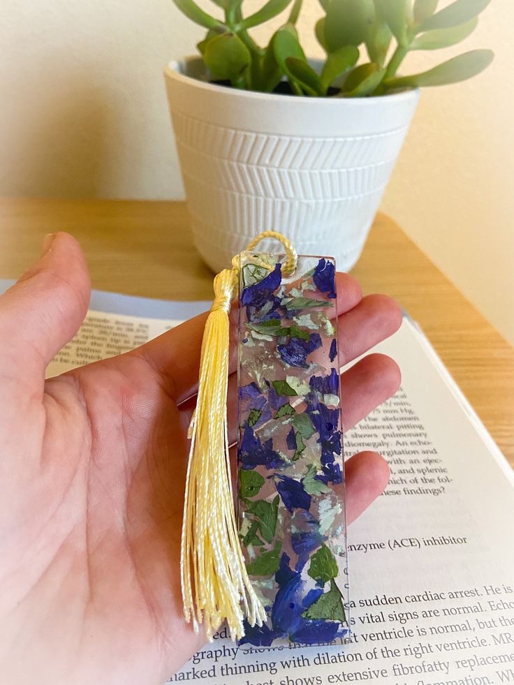 a hand holding a small piece of glass with flowers on it next to a potted plant