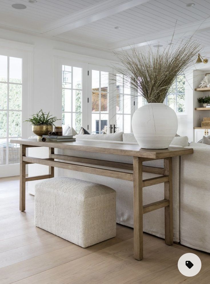 a white vase sitting on top of a wooden table next to a bench in a living room