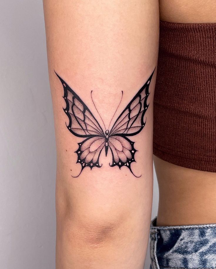 a woman's arm with a black and white butterfly tattoo on the left side