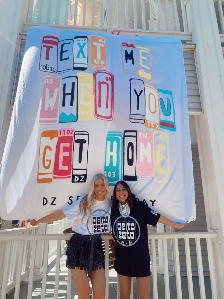 two girls holding up a large sign with letters on it and the words get home written across them