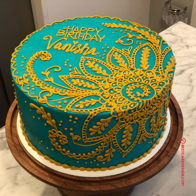 a blue and gold decorated birthday cake on a wooden stand with white marble countertop