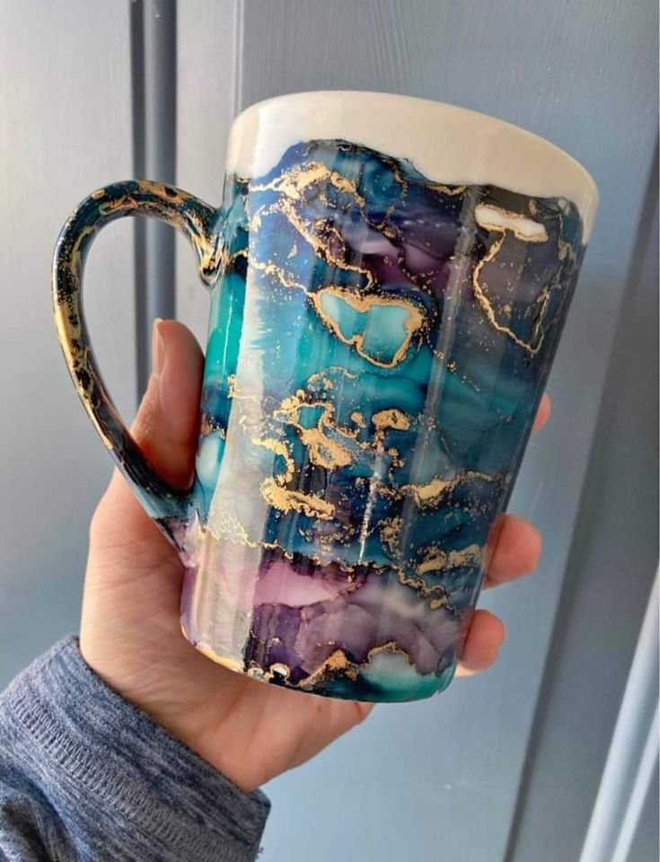 a hand holding a coffee cup with gold and blue designs