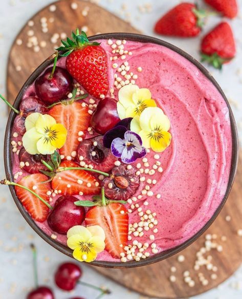 a smoothie topped with strawberries, cherries and flowers on a wooden board