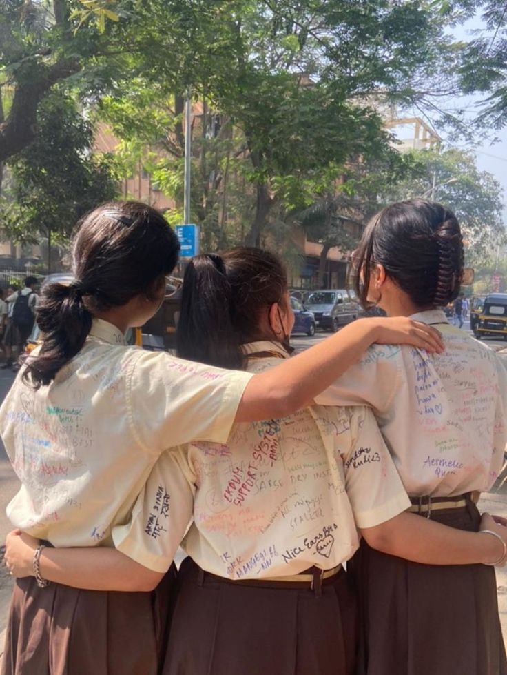 three girls in school uniforms are hugging each other on the street with writing all over them