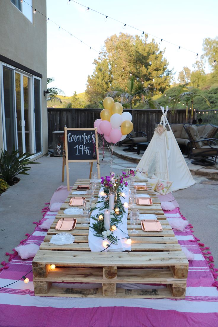 a table set up for a party with pink and white striped linens, balloons and candles