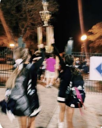 two girls are walking down the sidewalk with their arms in the air