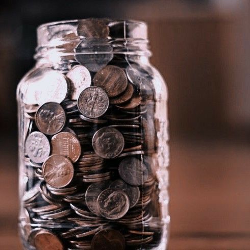 a glass jar filled with coins sitting on top of a wooden table