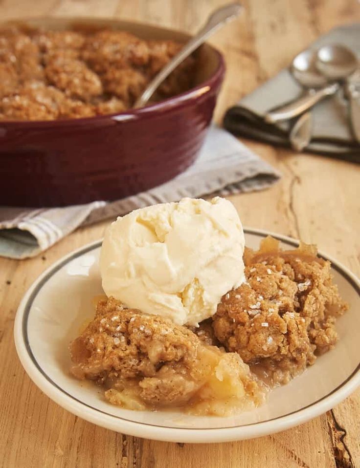 two pieces of apple crisp on a plate with ice cream and spoons next to it