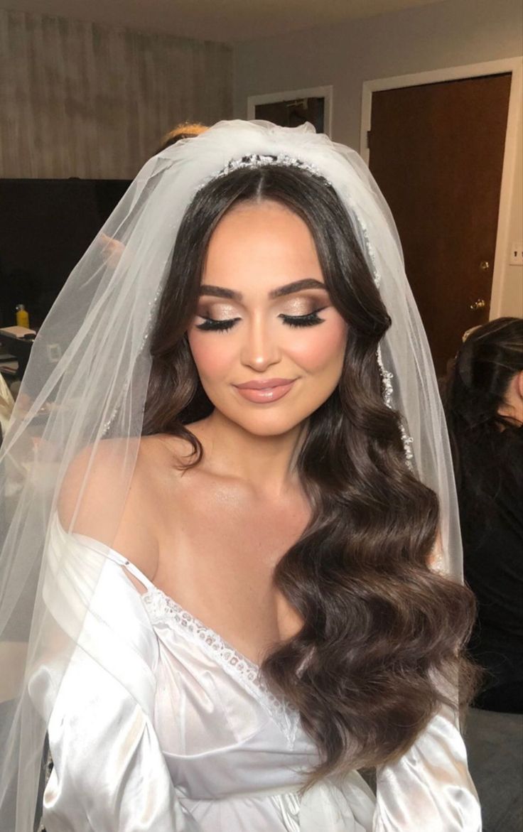 a woman wearing a wedding veil with long dark hair and makeup on her face is looking at the camera