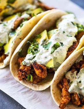 three tacos with chicken, sauce and green onions on paper towel next to each other