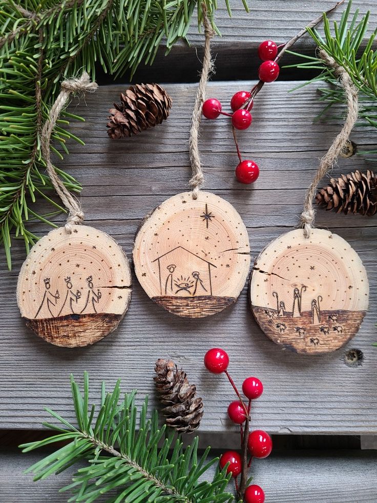 three wooden ornaments with nativity scene on them and pine cones hanging from the branches