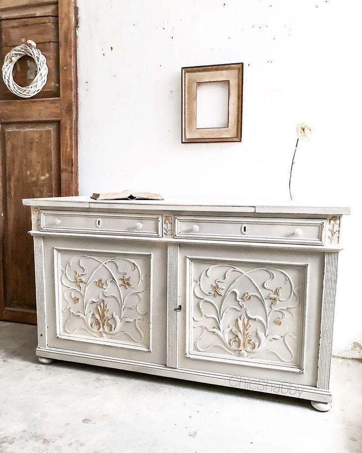 an old dresser is painted white and has ornate carvings on the front, along with a wreath