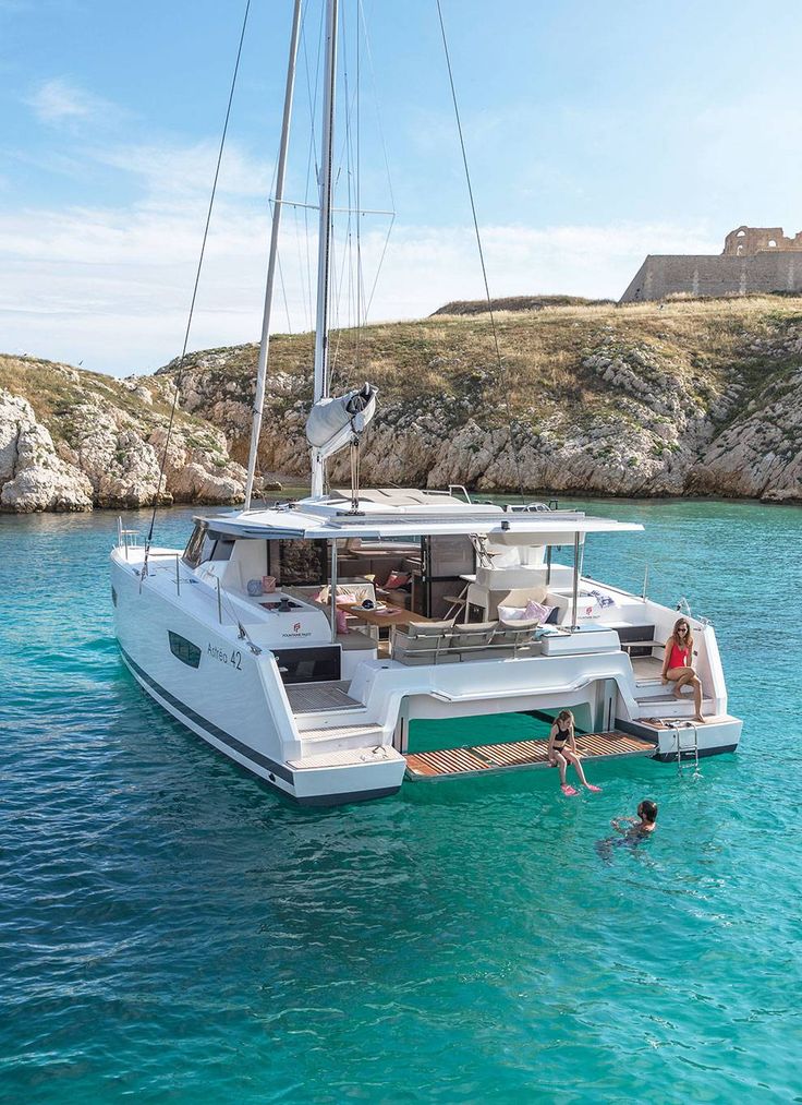 two people swimming in the ocean near a catamaran boat with a man and woman on it